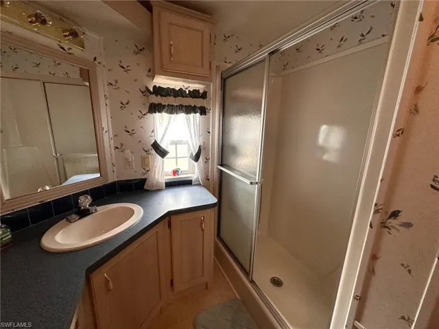 Bathroom with wallpapered walls, vanity, a shower stall, and tile patterned floors