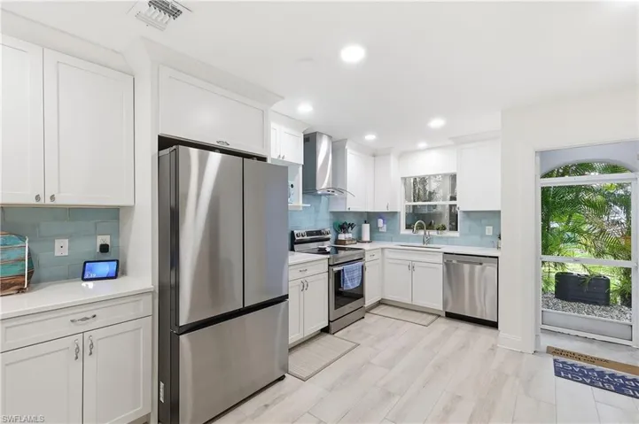 Kitchen with stainless steel appliances, white cabinets, backsplash, recessed lighting, and light stone counters