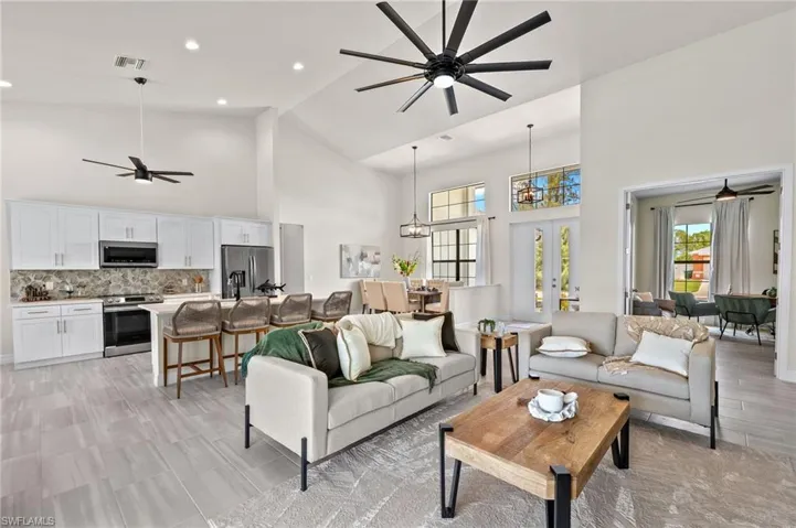 Living room with high vaulted ceiling, french doors, ceiling fan, and light tile floors