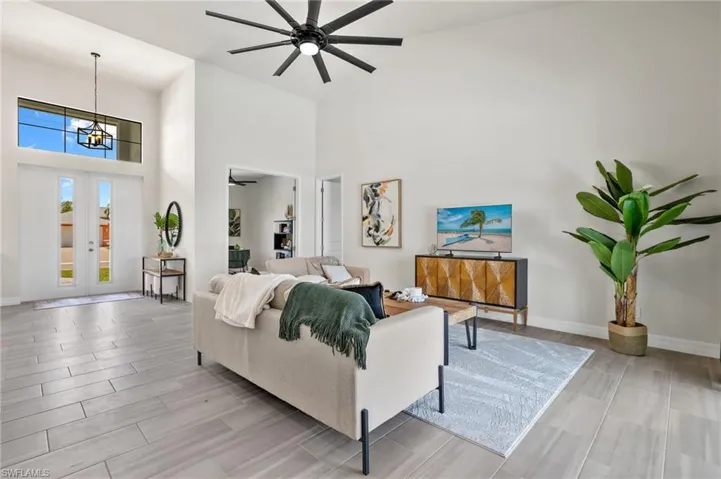 Living room featuring a high ceiling, ceiling fan with notable chandelier, and french doors