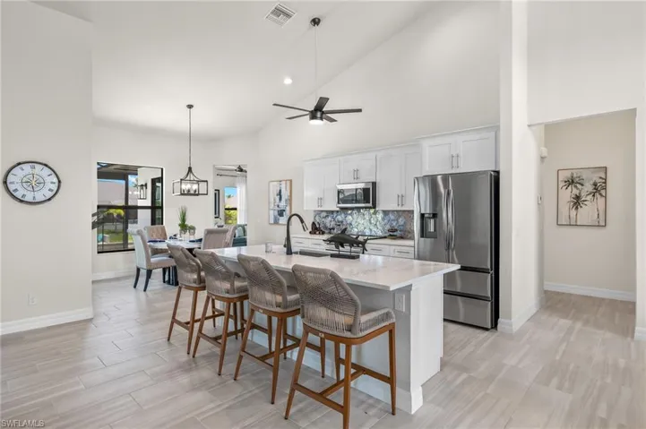Kitchen with tasteful backsplash, a center island with sink, pendant lighting, high vaulted ceiling, and appliances with stainless steel finishes