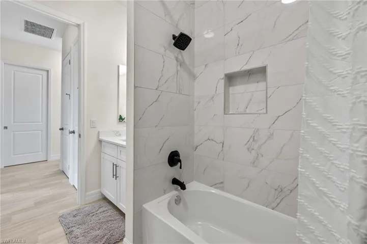 Bathroom with hardwood / wood-style flooring, tiled shower / bath combo, and vanity