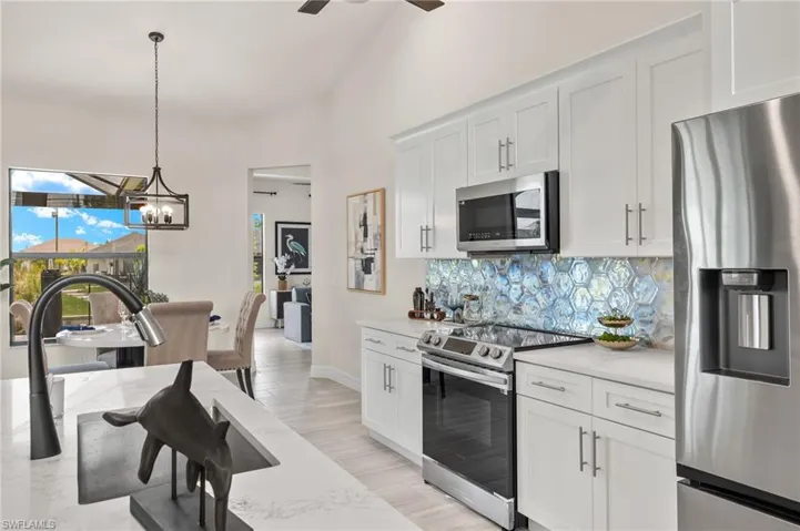 Kitchen with light hardwood / wood-style floors, tasteful backsplash, stainless steel appliances, pendant lighting, and ceiling fan with notable chandelier