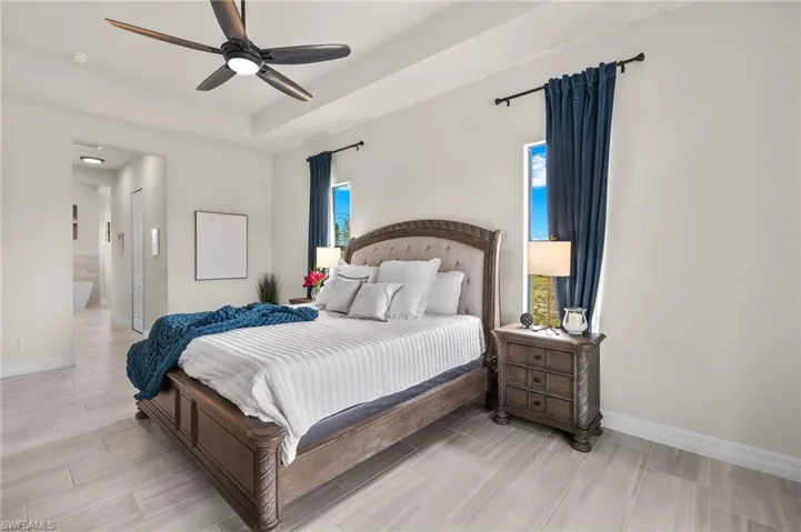Bedroom with ensuite bathroom, ceiling fan, and a tray ceiling