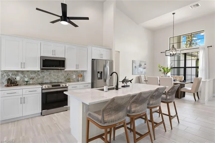 Kitchen with a kitchen breakfast bar, appliances with stainless steel finishes, white cabinets, pendant lighting, and high vaulted ceiling