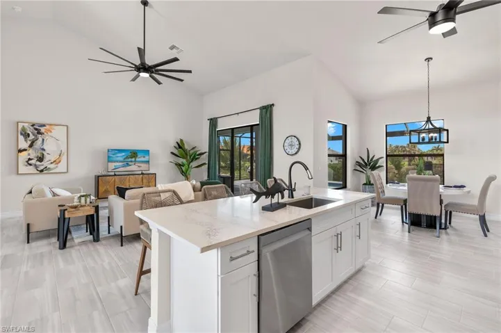 Kitchen featuring hanging light fixtures, ceiling fan with notable chandelier, a kitchen island with sink, and stainless steel dishwasher