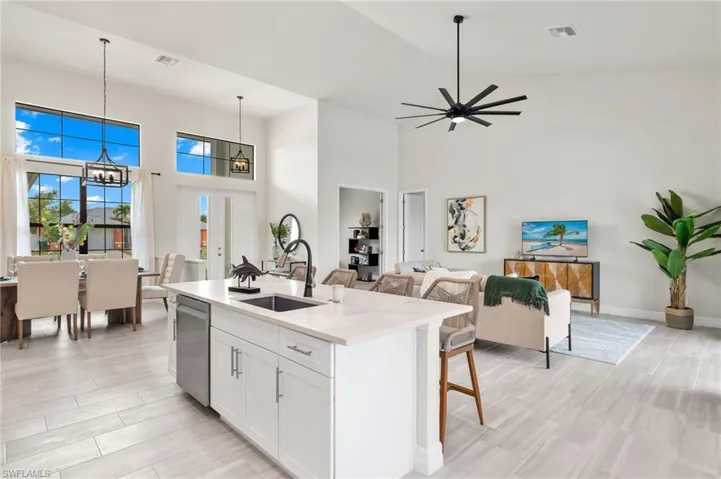 Kitchen with light stone countertops, a kitchen island with sink, pendant lighting, high vaulted ceiling, and sink