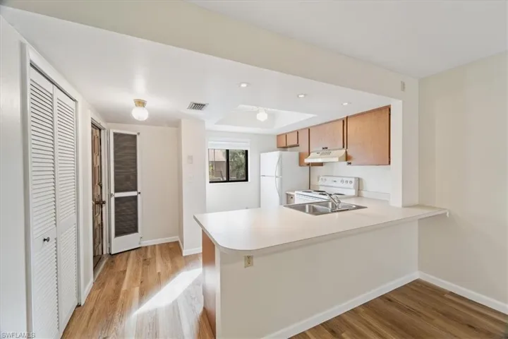 Kitchen with light hardwood / wood-style flooring, kitchen peninsula, sink, and white appliances