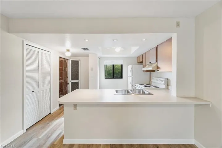 Kitchen with white appliances, light wood-type flooring, sink, and kitchen peninsula