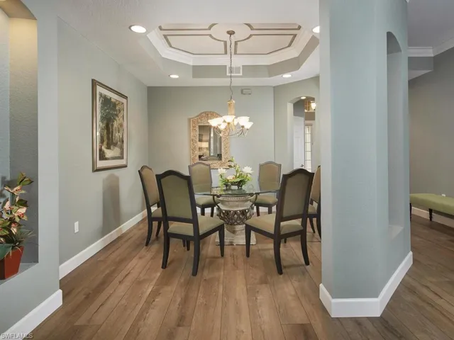 Dining space with arched walkways, crown molding, hardwood / wood-style floors, a chandelier, and a tray ceiling