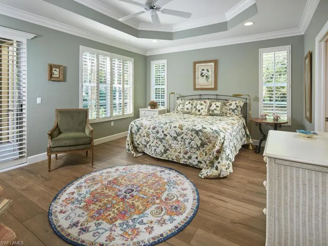 Bedroom with a raised ceiling, crown molding, hardwood / wood-style flooring, a ceiling fan, and access to outside