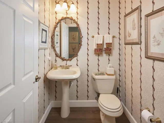 Half bath with dark wood-type flooring and wallpapered walls