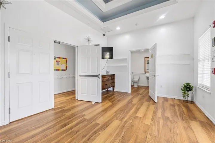 Unfurnished bedroom with connected bathroom, light wood finished floors, a chandelier, and a tray ceiling