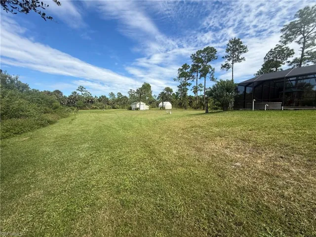 View of grassy yard featuring a sunroom, a lanai, and an outbuilding
