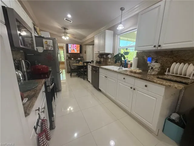 Kitchen with ornamental molding, dark stone counters, white cabinets, light tile patterned floors, and ceiling fan
