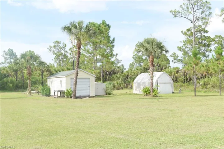 View of green lawn with a shed and view of wooded area