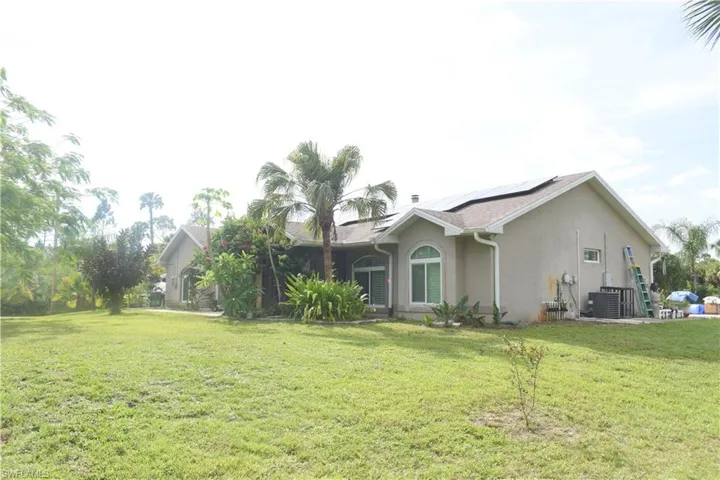View of side of property with roof mounted solar panels, stucco siding, and a yard