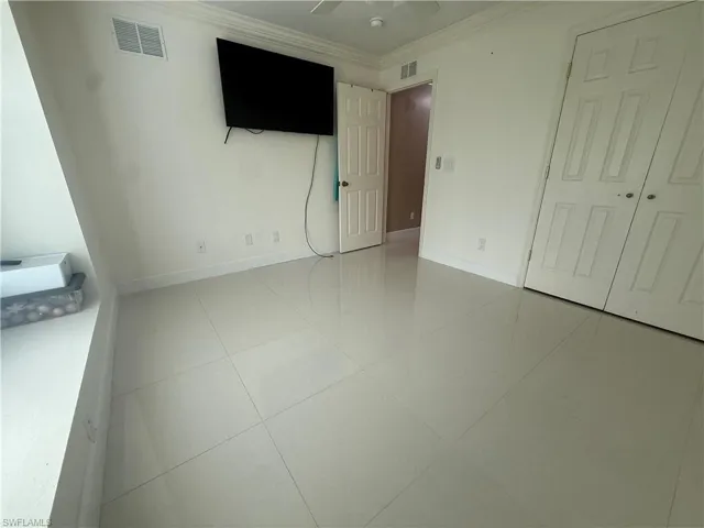 Unfurnished bedroom featuring crown molding, light tile patterned floors, and a ceiling fan