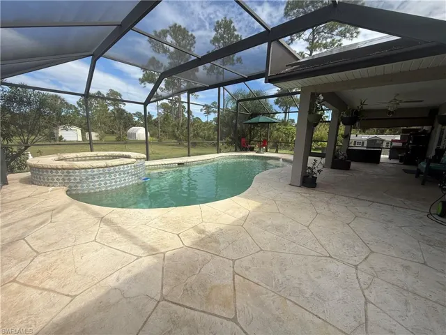 View of swimming pool featuring a patio, glass enclosure, a ceiling fan, a pool with connected hot tub, and a sunroom
