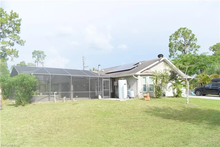 Rear view of house with solar panels, a yard, glass enclosure, water heater, and stucco siding