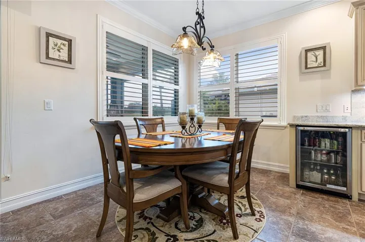 Tiled dining area with beverage cooler, a notable chandelier, and ornamental molding
