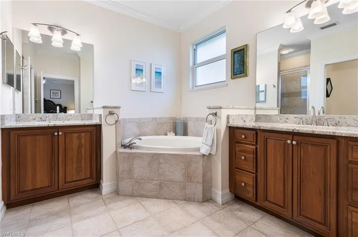 Owners Bathroom with tile flooring, dual oversized vanity, tiled tub, and crown molding