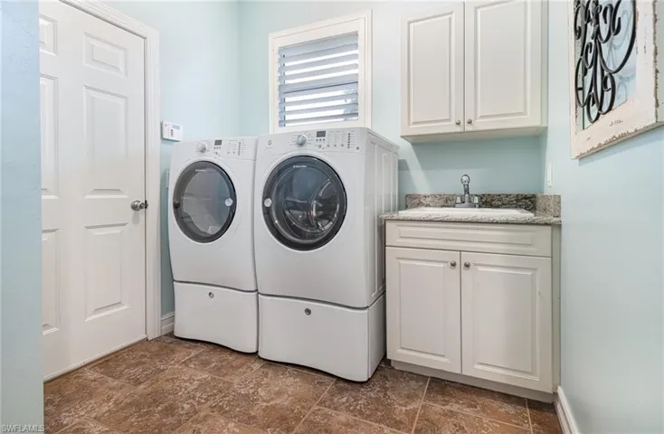 Laundry room featuring washer and clothes dryer, sink, dark tile flooring, and cabinets