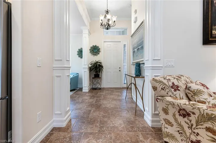 Entryway with a notable chandelier, dark tile flooring, decorative columns, and ornamental molding