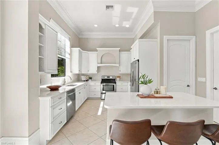 Kitchen featuring crisp white shaker-style cabinetry, a central island with a quartz countertop, stainless steel appliances, crown molding, and neutral tile flooring