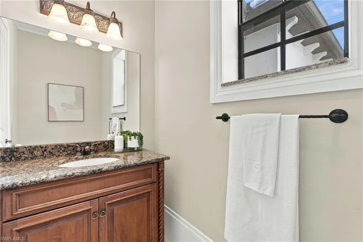 Wood-finish cabinetry with decorative rope-style columns, stone-surface countertop with an integrated oval sink, full-width mirror, multi-light fixture, and black finish hardware