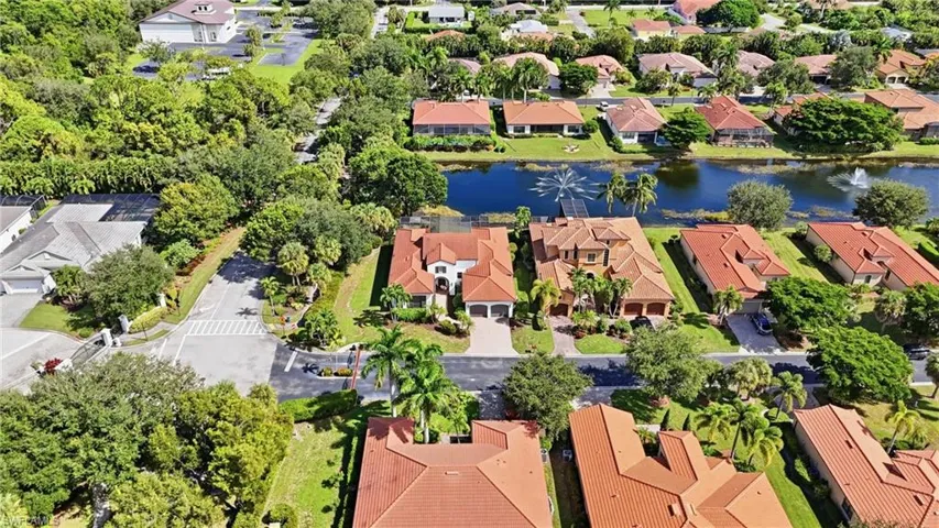 Aerial perspective featuring a multi-story residence with a clay tile roof, paved driveway, attached garage, and landscaped grounds situated on a waterfront lot
