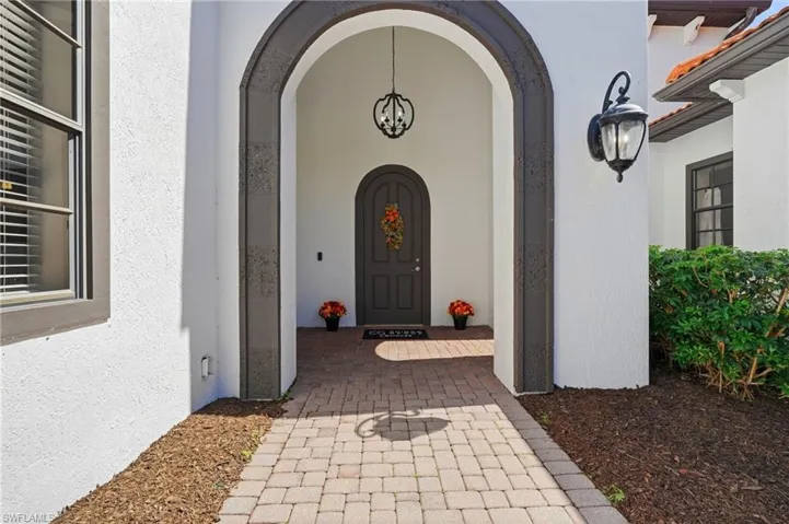Stucco exterior featuring an arched entryway with stone-textured detailing, brick-paver walkway, arched front door, and metal exterior light fixtures