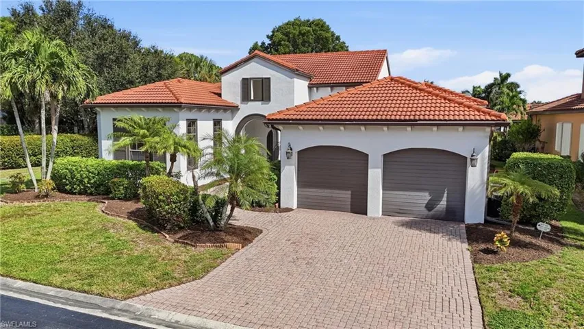Mediterranean-style exterior featuring a clay tile roof, stucco facade, arched dual-car garage, and a brick-paver driveway