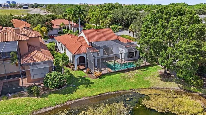 Single-story residence featuring a terra-cotta tile roof, a screened-in lanai with a private pool, and water frontage with manicured landscaping