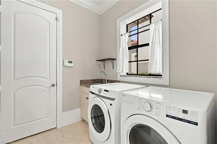 Laundry room featuring a stone-surface countertop, integrated sink with a gooseneck faucet, custom cabinetry, tiled flooring, and a multi-pane window