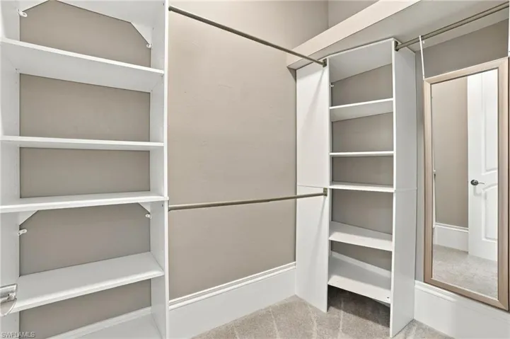 Custom walk-in closet featuring white built-in shelving towers, metallic hanging rods, and a wall-mounted mirror