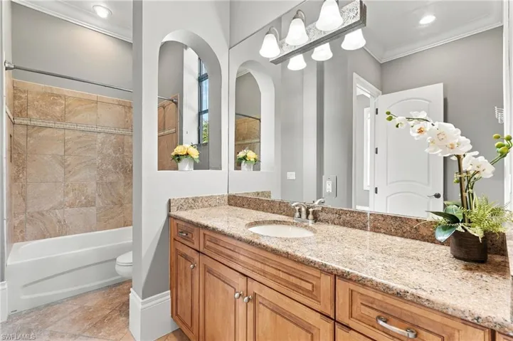Bathroom featuring wood cabinetry, stone countertop with integrated sink, full-height wall mirror, arched wall alcoves, and a tiled shower surround