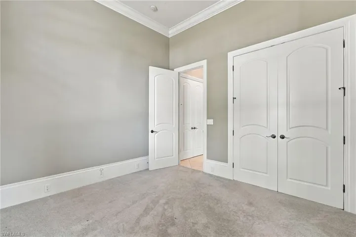 Room featuring neutral wall tones, crown molding, plush carpeting, and white arched-panel interior doors with dark hardware