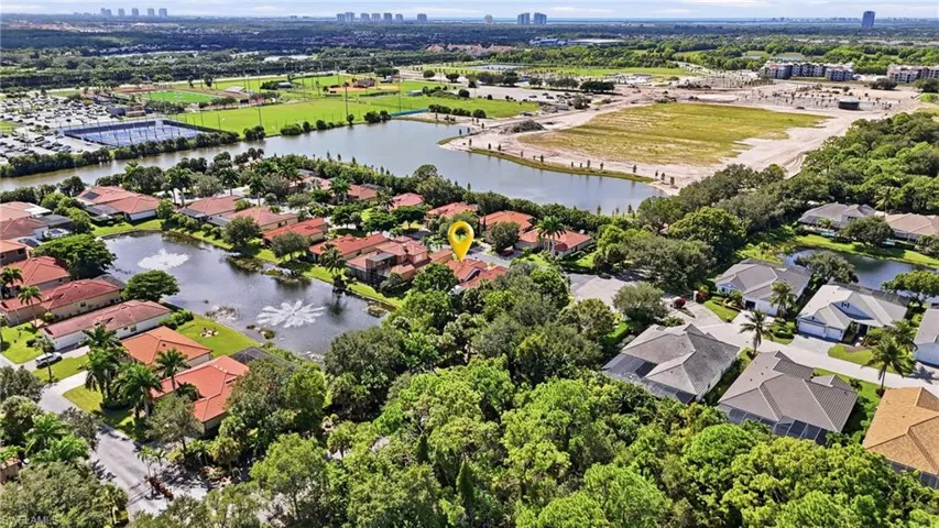 Aerial perspective of residential property featuring a clay-tiled roof, waterfront positioning, mature landscaping, and an expansive treed canopy