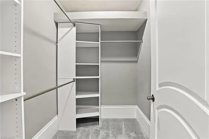 Walk-in closet featuring white built-in shelving, integrated hanging rods, grey wall-to-wall carpeting, and a multi-panel door