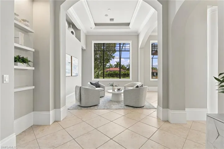 Formal living area featuring arched architectural entryways, high tray ceilings, large windows with black frames, and custom built-in shelving, finished with tile flooring