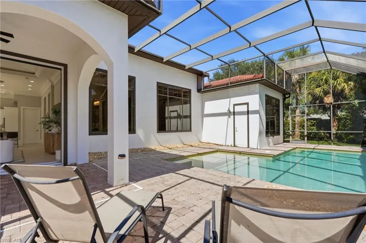 Screened-in patio featuring a paver deck and an integrated swimming pool, framed by an arched covered entry and large glass windows