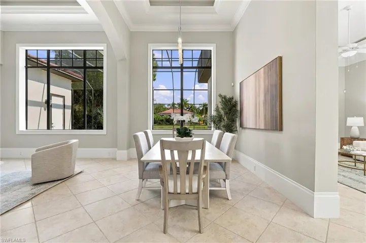 Dining area featuring high ceilings with crown molding, tray ceiling detail, large windows with black framing, tile flooring, and a linear pendant light fixture