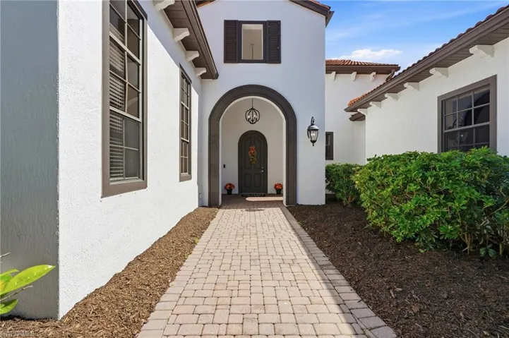 Stucco exterior entry featuring a paved stone walkway, arched entryway, dark-toned shutters, and wall-mounted exterior lanterns