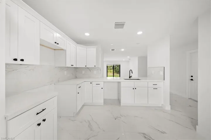 Kitchen with a sink, recessed lighting, light marble finish flooring, white cabinets, and decorative backsplash