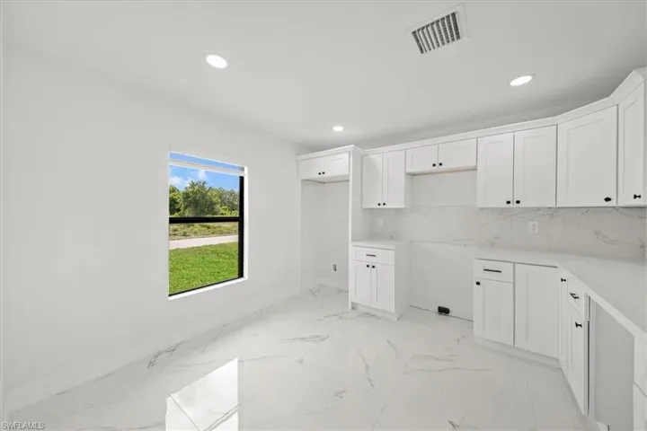 Kitchen featuring baseboards, recessed lighting, white cabinetry, light marble finish floors, and tasteful backsplash