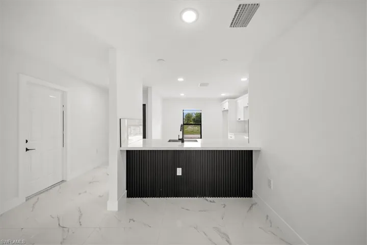 Kitchen featuring white cabinets, light marble finish floors, baseboards, a sink, and recessed lighting