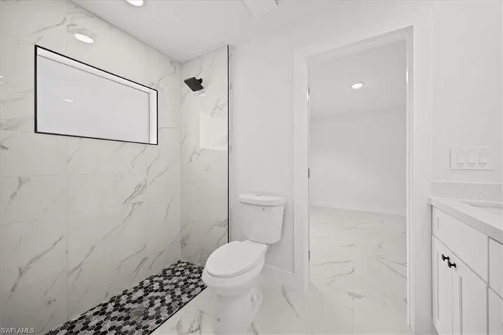 Full bathroom featuring marble finish floors, toilet, vanity, a marble finish shower, and baseboards