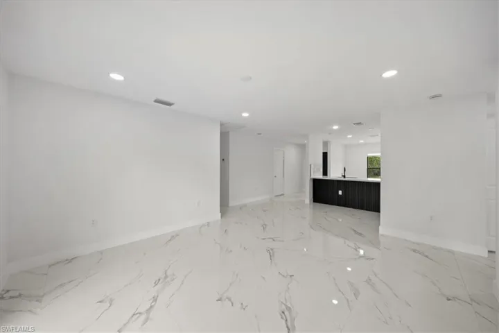 Unfurnished living room with recessed lighting, baseboards, light marble finish floors, and a sink