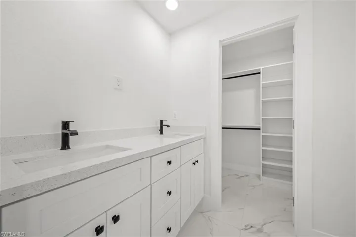 Full bath with marble finish floors, double vanity, and a walk in closet